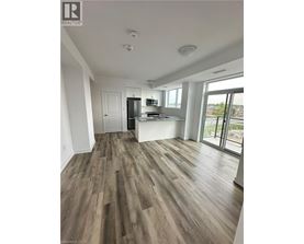 A spacious room with wood flooring and a kitchen area in the background.