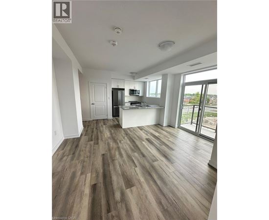 A spacious room with wood flooring and a kitchen area in the background.