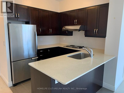 A kitchen with a stainless steel refrigerator and dark brown cabinets.