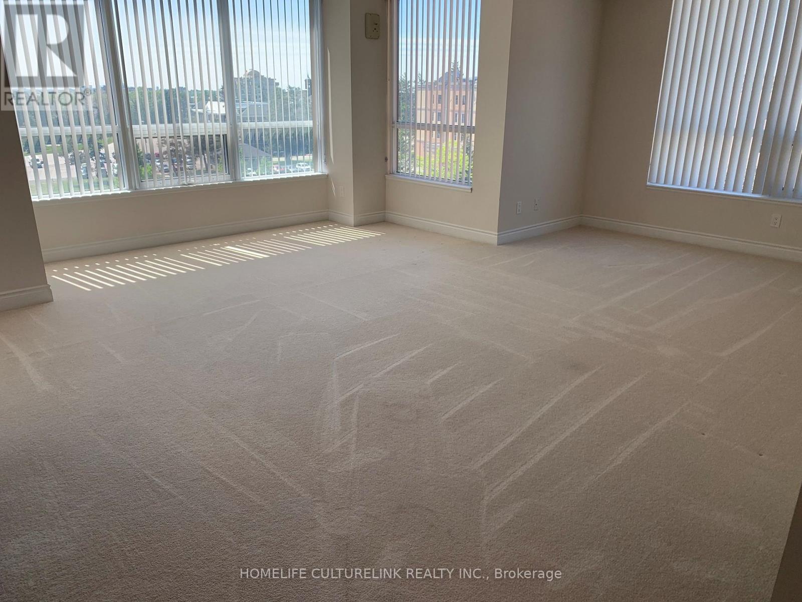A room with a carpeted floor and a large window with blinds.