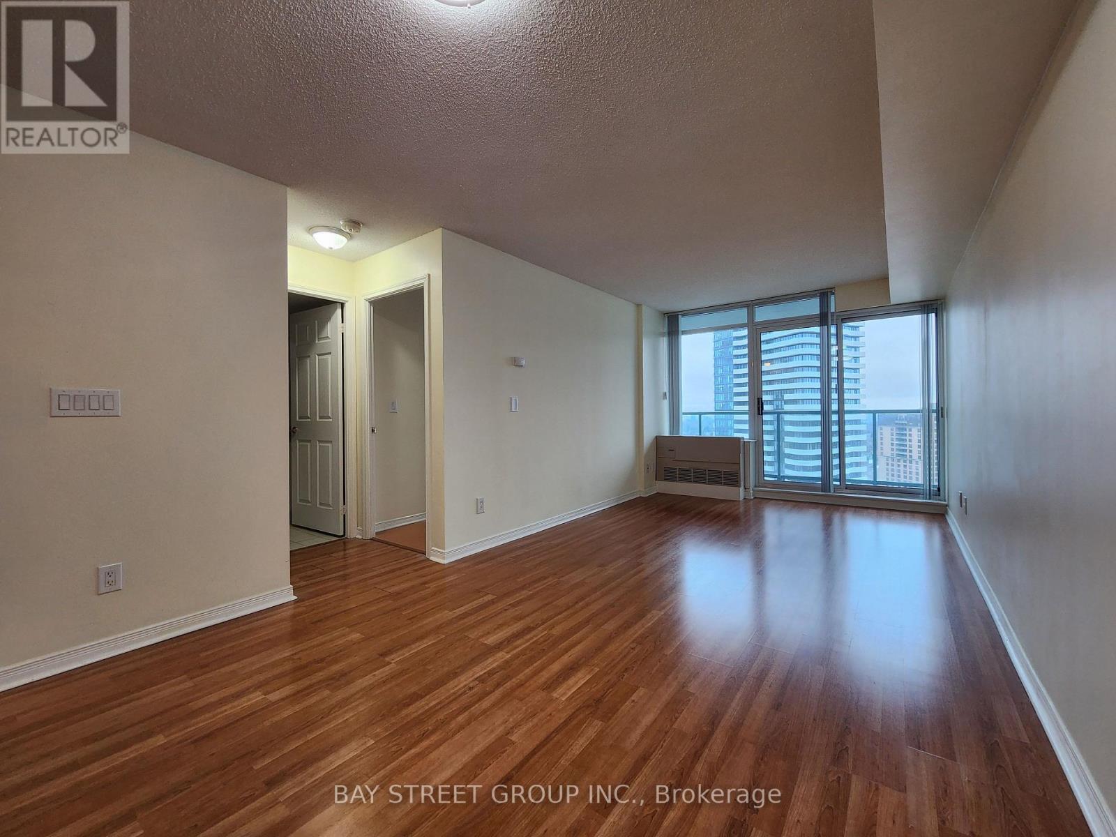 A spacious room with wooden flooring and a sliding glass door leading to a balcony.