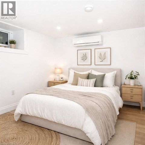 A bedroom with a large bed, a nightstand with a lamp, and two framed leaves on the wall.
