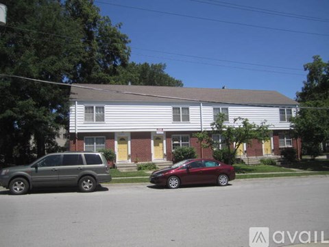 A red car is parked in front of a white building with a yellow door.