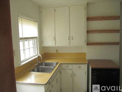 A kitchen with white cabinets and a wooden shelf above the sink.