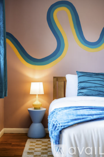 A bedroom with a bed, lamp, and a wall mural.