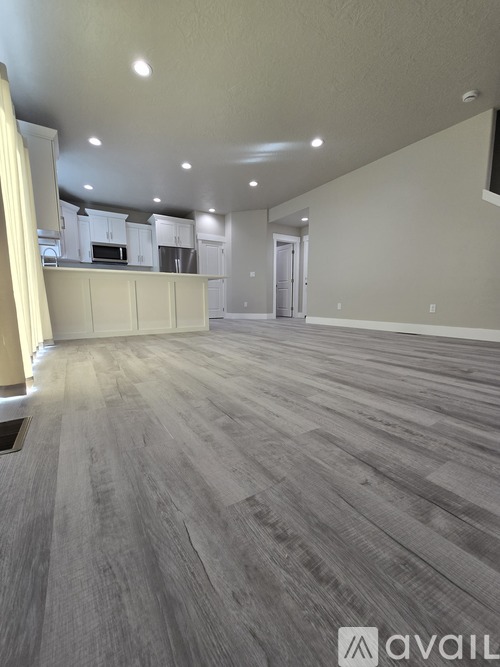 A spacious room with wooden flooring and a kitchen area in the background.