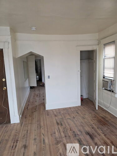 A room with wooden floors and white walls, with a doorway leading to another room.
