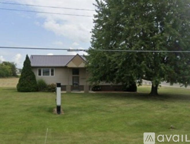 A house with a brown roof and a white fence is surrounded by a grassy yard.