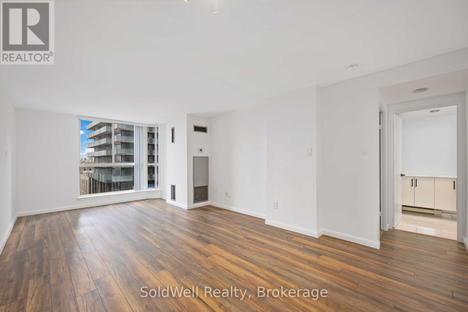 A spacious room with wooden flooring and white walls, with a sliding glass door leading to a balcony.