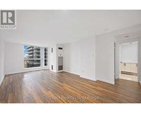 A spacious room with wooden flooring and white walls, with a sliding glass door leading to a balcony.