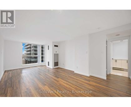 A spacious room with wooden flooring and white walls, with a sliding glass door leading to a balcony.