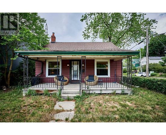 A small red house with a porch and a green lawn.