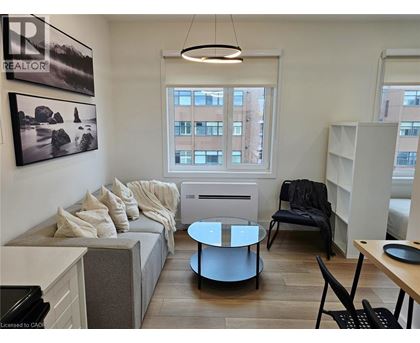 A living room with a grey couch, a black chair, and a round glass table.
