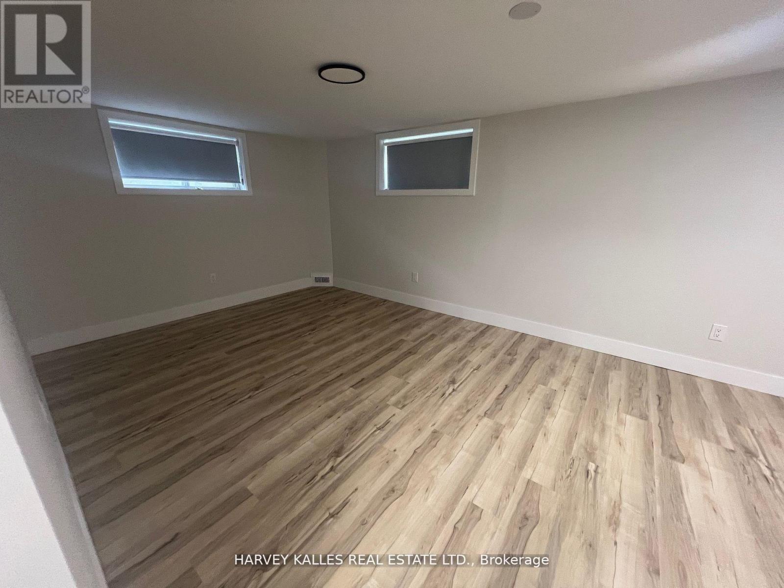 A room with wooden flooring and two windows.