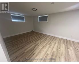 A room with wooden flooring and two windows.
