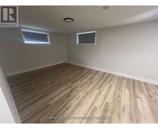 A room with wooden flooring and two windows.