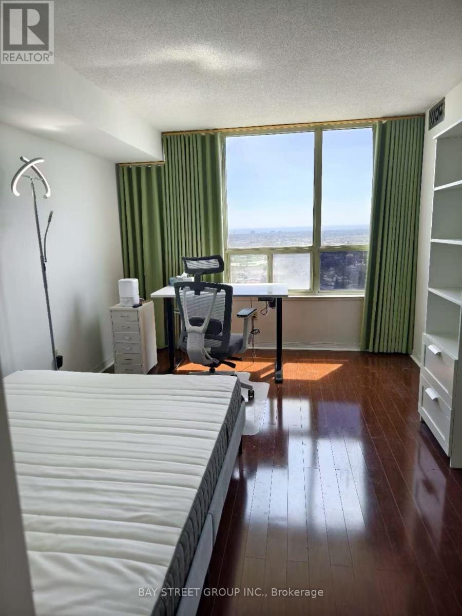 A bedroom with a bed, desk, and chair with a window overlooking the city.