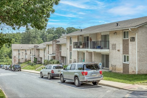 A silver SUV is parked on the side of a street in front of a brick apartment building.