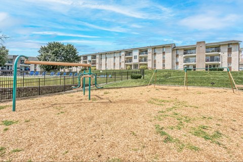 A playground with a green slide and a brown sandbox in front of apartment buildings.