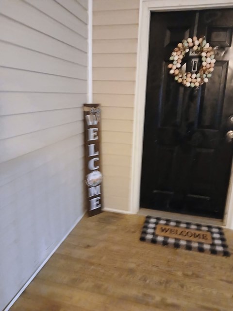 A black door with a wreath and a welcome mat.