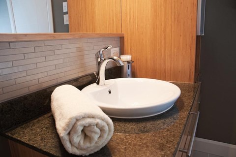 A white towel is folded into a heart shape and placed on a granite countertop next to a white sink.