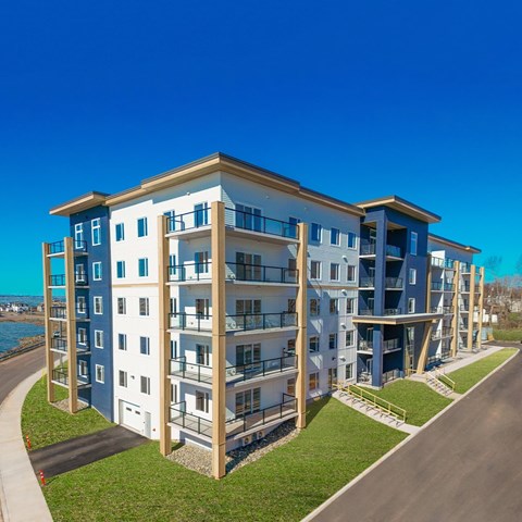 A modern multi-story residential building with balconies and a clear blue sky in the background.