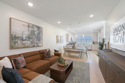 A living room with a brown couch and a painting on the wall.