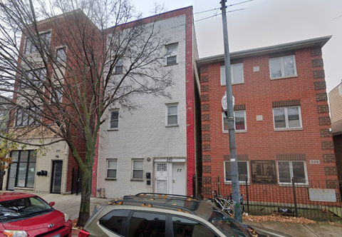 A red car is parked in front of a grey and red building.