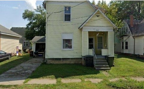 A yellow house with a porch and a car parked in front.