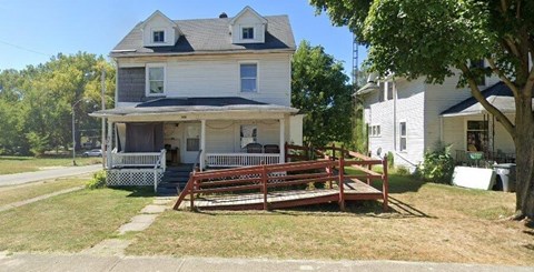 A white house with a porch and a tree in front.