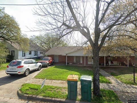 A tree in front of a house with a white car parked in front of it.
