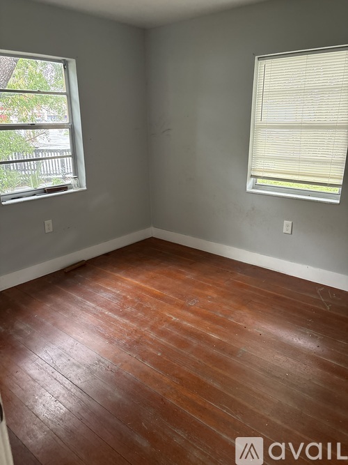 A room with wooden flooring and two windows.