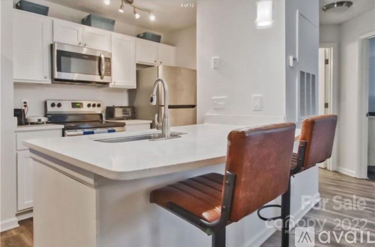 A kitchen with white cabinets and a white countertop with a sink and two brown chairs.
