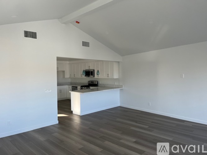 A spacious room with a kitchen in the background and a wooden floor.