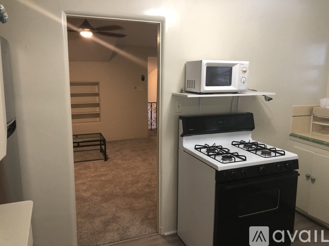A small kitchen with a stove and a microwave on a shelf.