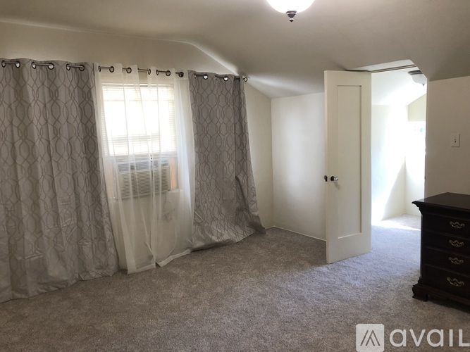 A room with a carpeted floor, a window with curtains, a door, and a dresser.