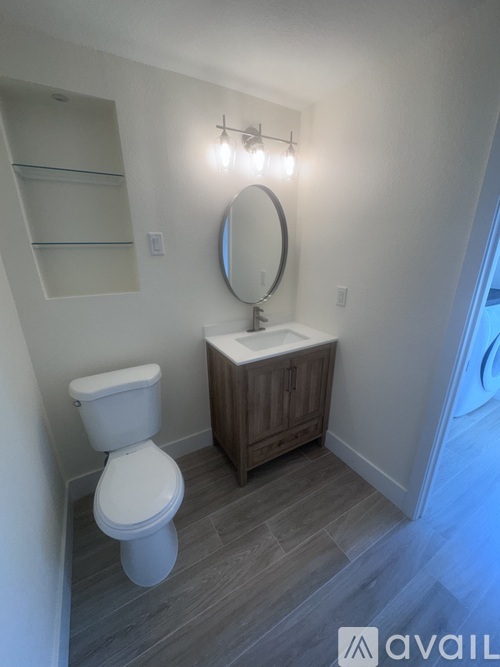 A bathroom with a toilet, sink, mirror, and shelves.
