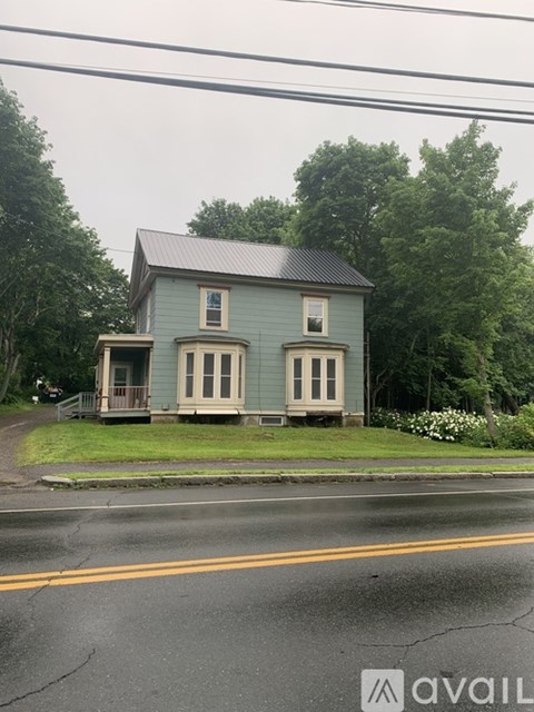 A blue house with a porch sits on the side of a road.