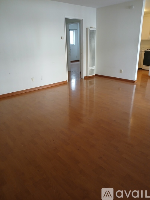 A room with wooden flooring and a doorway leading to another room.