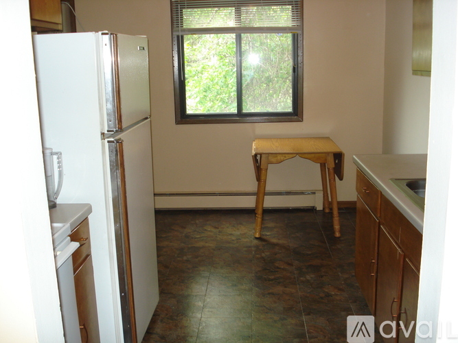 A kitchen with a white refrigerator, a window with a view of trees, and a wooden stool.