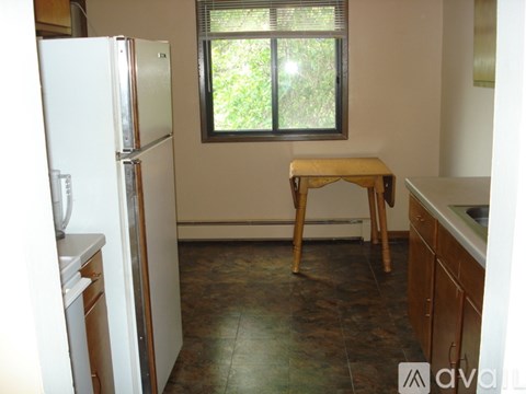 A kitchen with a white refrigerator, a window with a view of trees, and a wooden stool.
