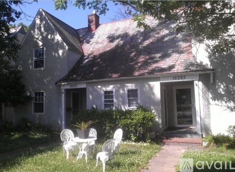 A white house with a red roof and a porch with chairs.