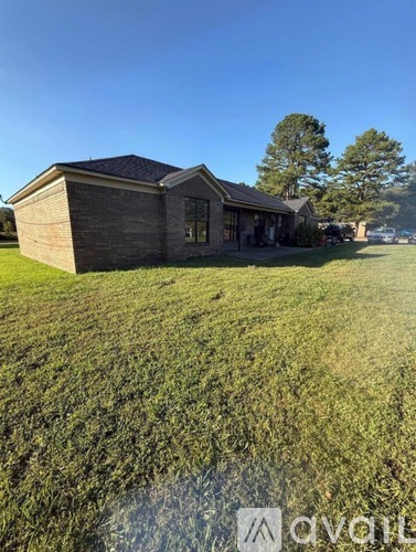 A house with a brown roof and a grey wall is surrounded by a grassy field.