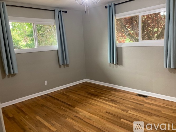 A room with wooden flooring and two windows with curtains.