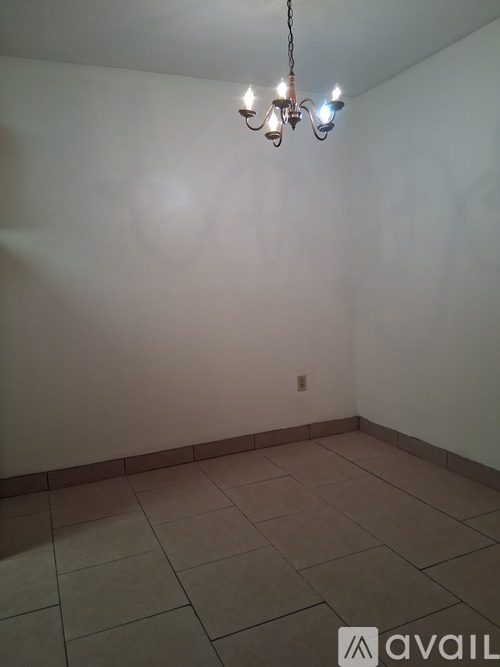A chandelier hangs from the ceiling in a room with white walls and tiled flooring.
