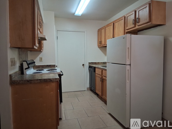 A kitchen with a white refrigerator, brown cabinets, and a white door.