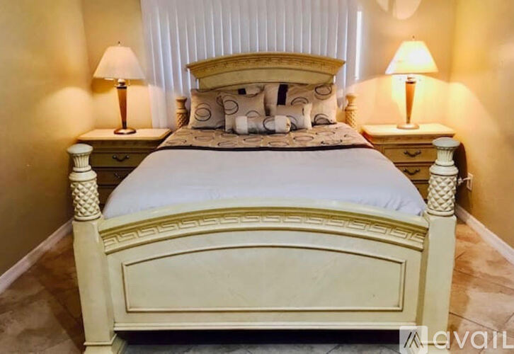 A bed with a white headboard and footboard is in a room with two lamps on either side.