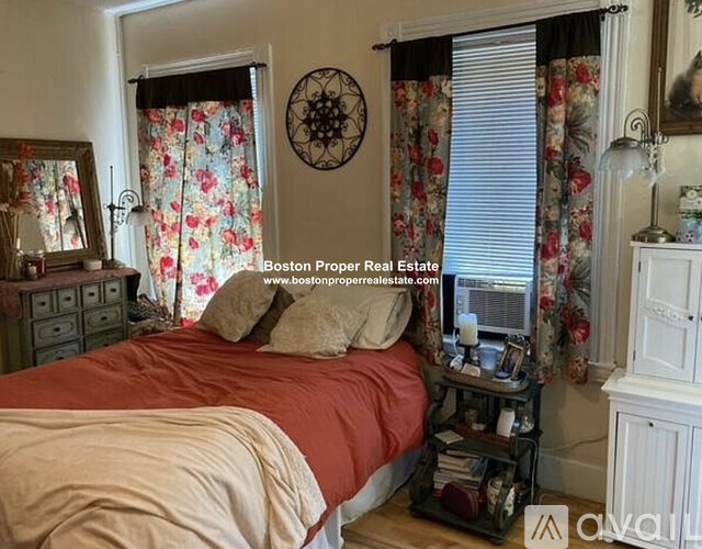 A bedroom with a bed, nightstand, and window with curtains.