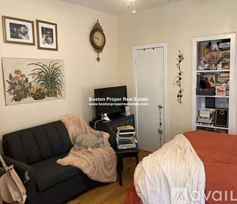 A living room with a black couch and a white bed.