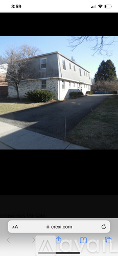 A white building with a grey roof is surrounded by a grassy area and a tree.